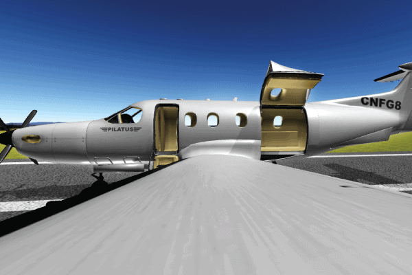 A Pilatus aircraft with its main and cargo doors open is parked on a runway under a clear blue sky, viewed from above the wing.
